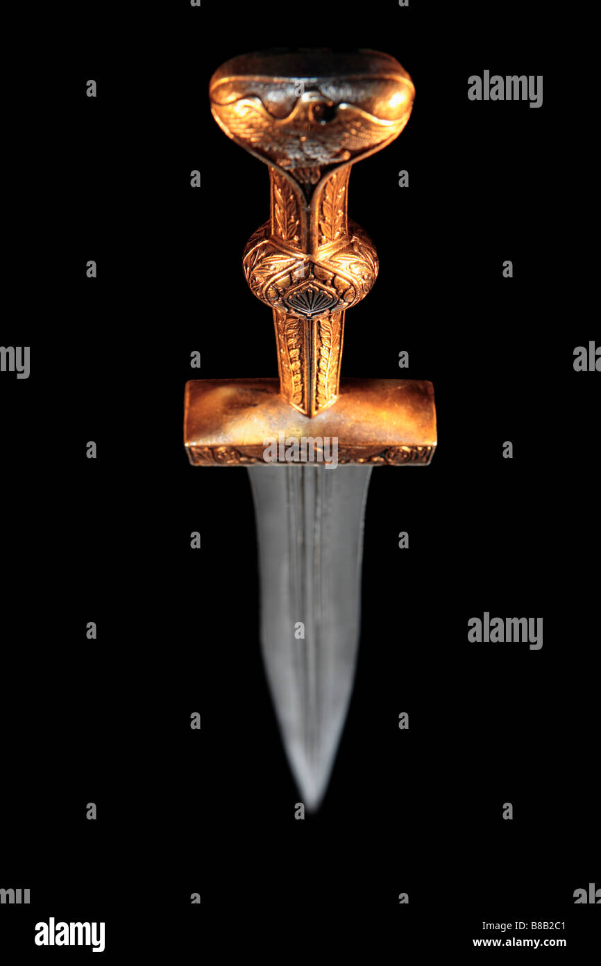 A replica Roman dagger with an eagle motif in a bronze handle set against a jet black background. Stock Photo