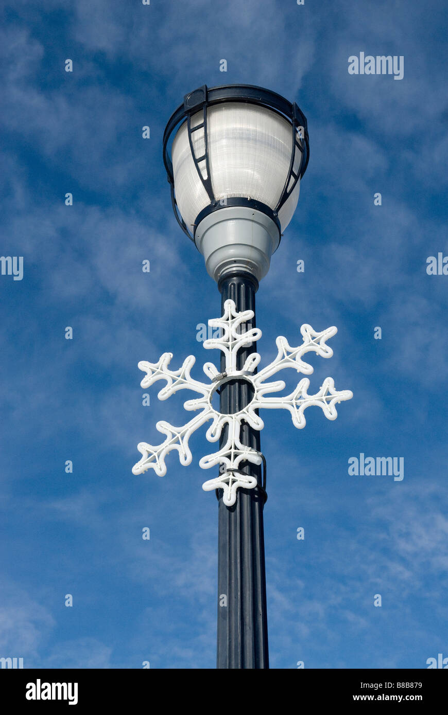 Streetlamp with large snowflake or Christmas ornament hanging from it, against a bright blue sky Stock Photo