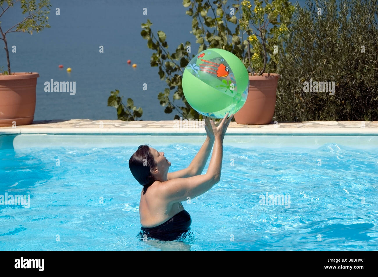 One women standing in swimming pool holding green beach ball above her head, sunny summer holiday Corfu, Kerkyra, Greece, Europe Stock Photo