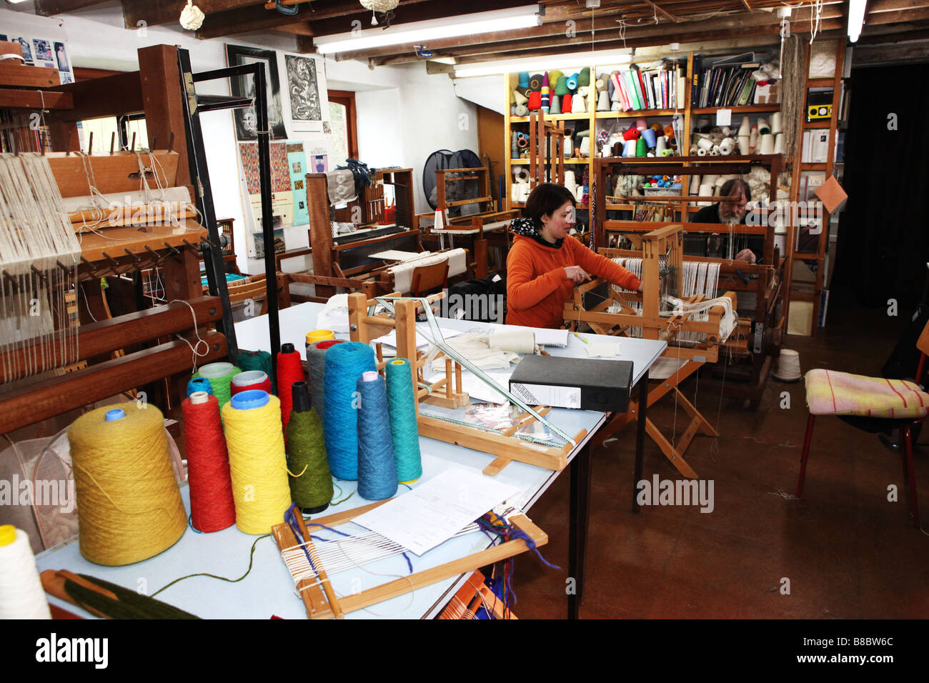 Two hand weavers working on small traditional wooden weaving machines