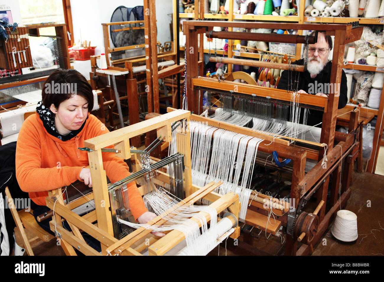 Two hand weavers working on small traditional wooden weaving machines
