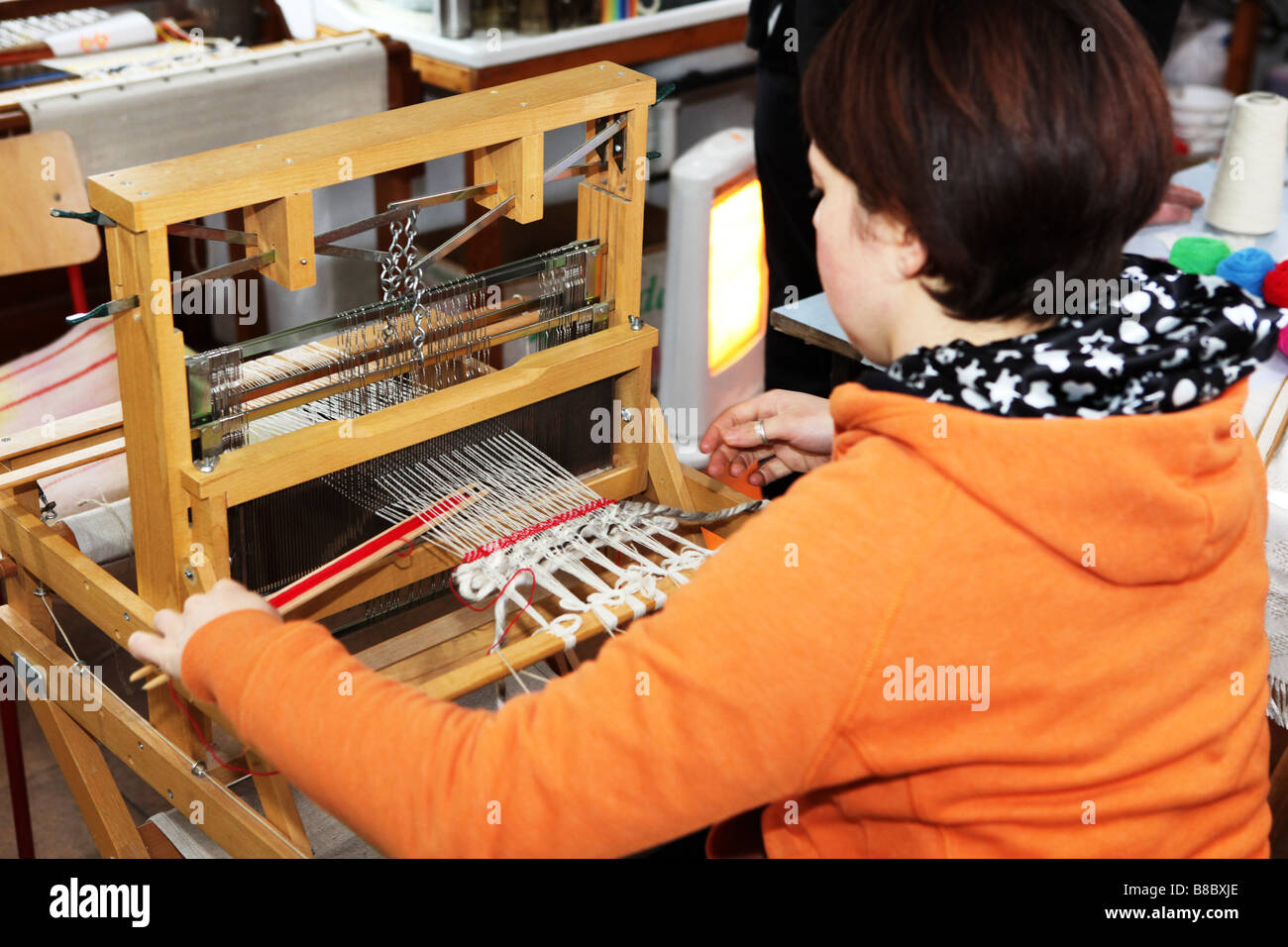 Hand weaver working on small traditional wooden weaving machine in a small textiles studio factory UK Stock Photo
