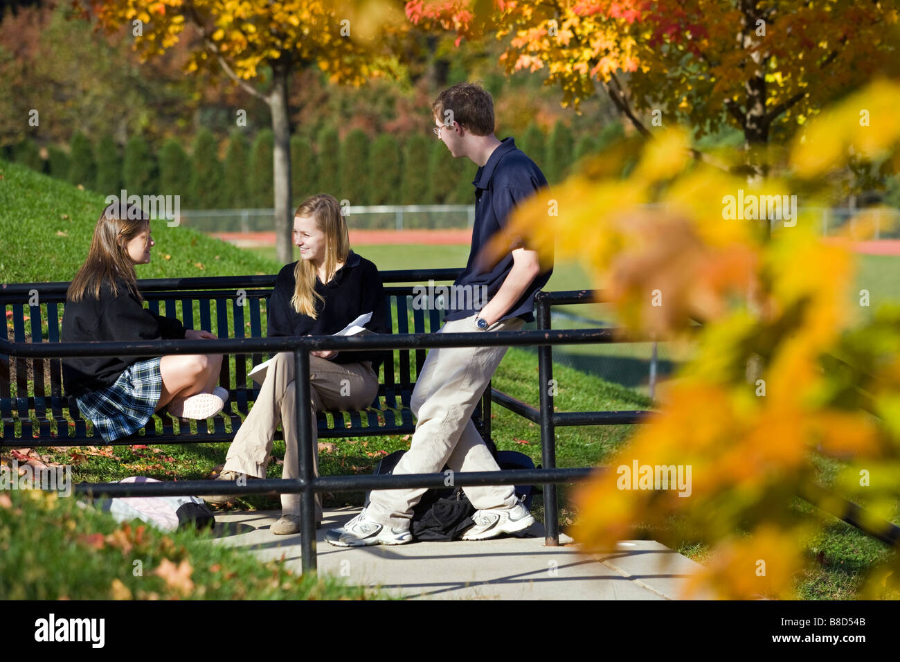 Two teenage girls and a boy chat on the campus of a private school. Stock Photo