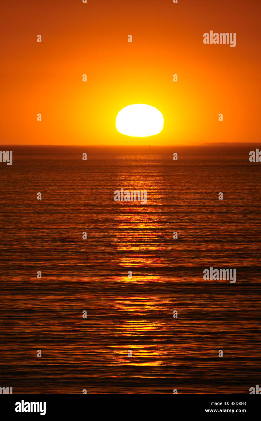The setting sun has almost reached the sharp horizon of the Pacific Ocean Stock Photo