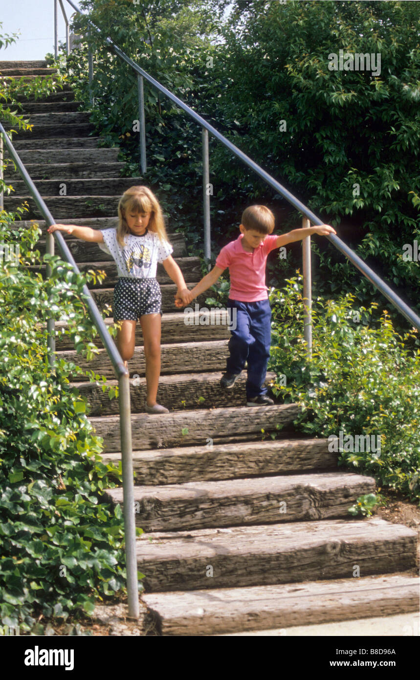 Young brother and sister descend wooden steps in city park love care support Stock Photo