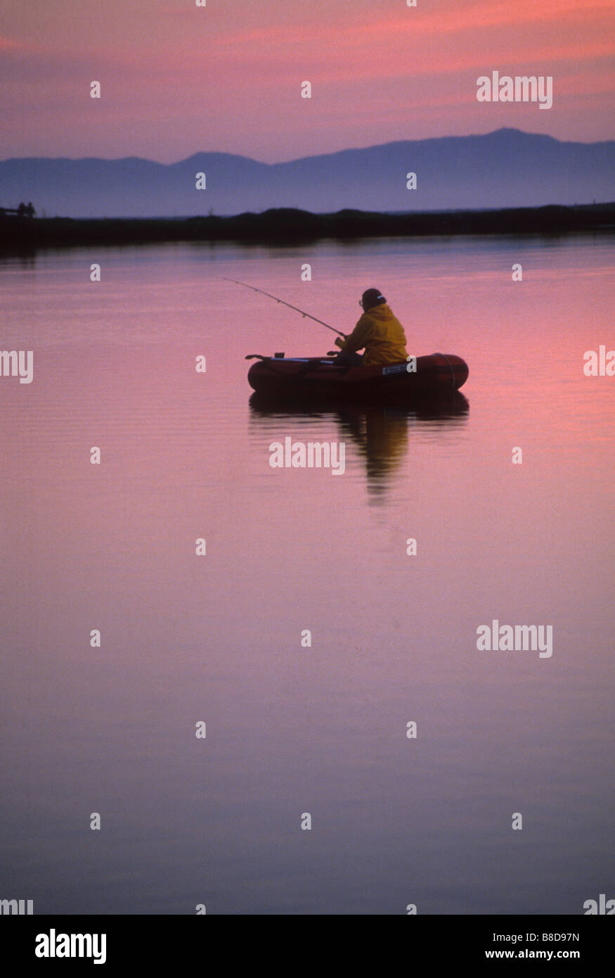 Lone fisherman in inflated boat floats on calm water at sunset Stock Photo