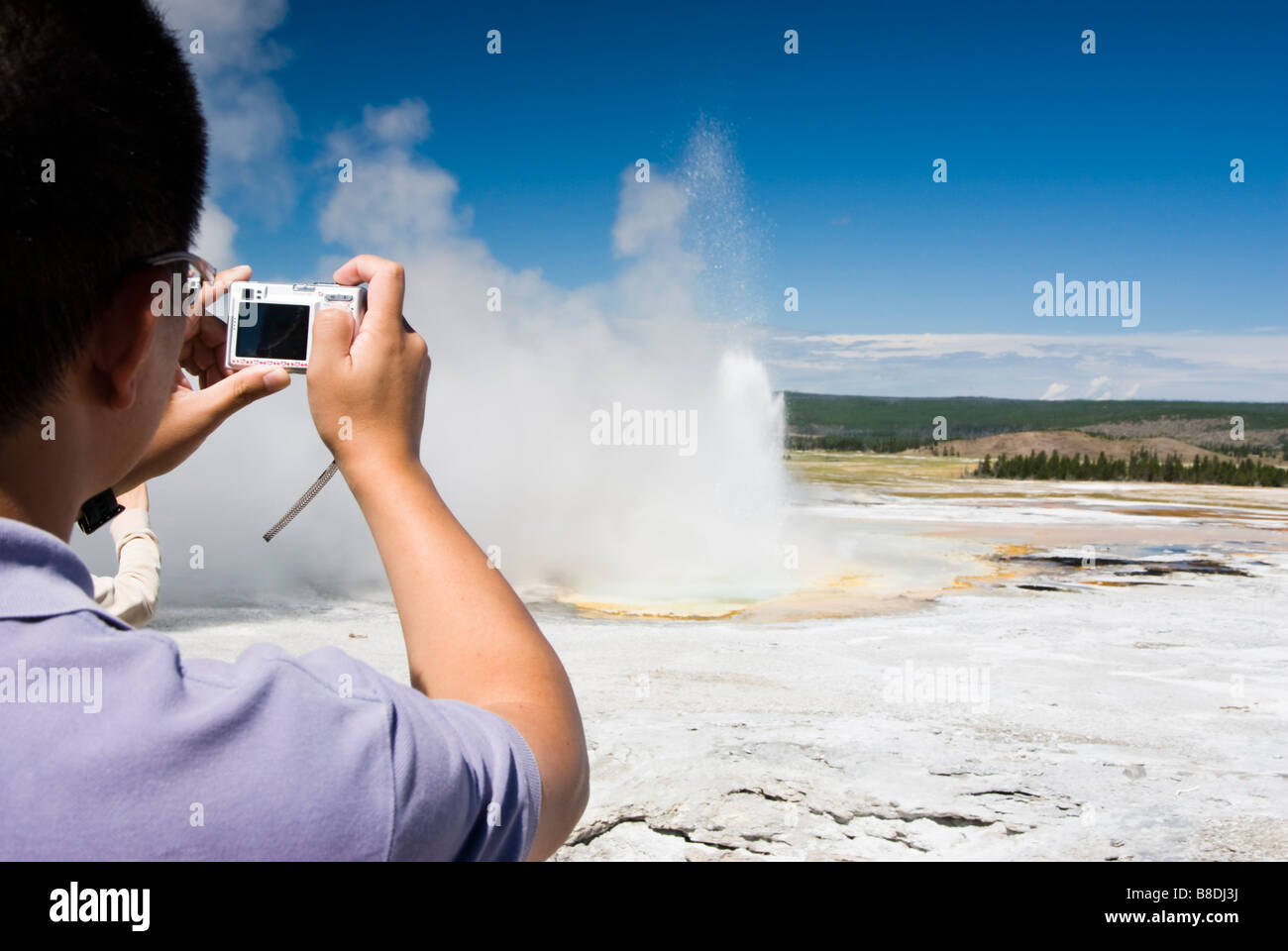 tourist photographing the Clepsydra geyser on the Fountain Paint Pot Trail in Yellowstone National Park Stock Photo