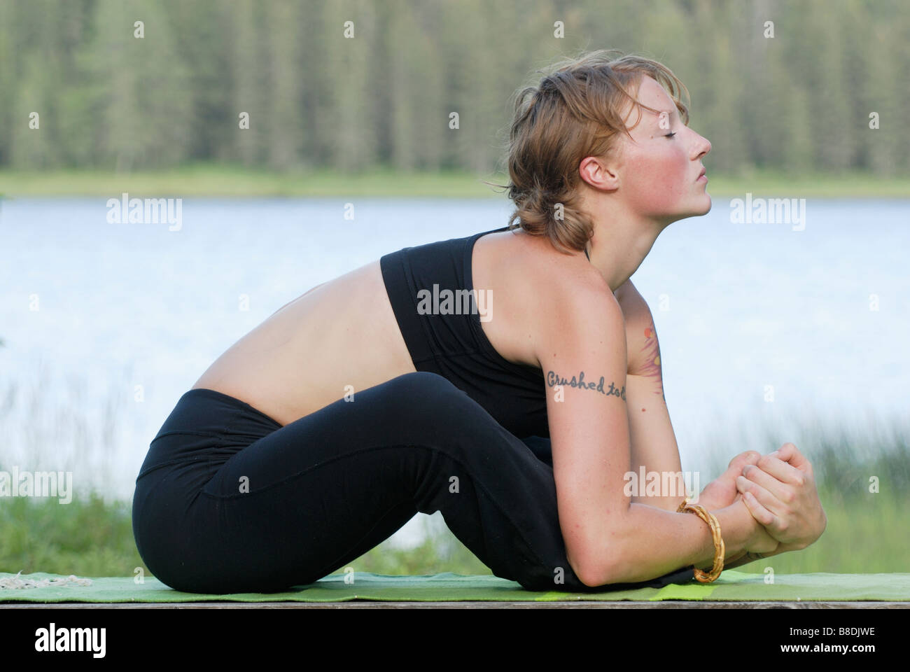 Woman exercising on yoga mat, beside Grayling Lake, Riding Mountain National Park, Manitoba, Canada Stock Photo