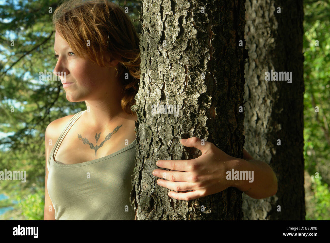 Woman with arm around tree, in a grove of trees, Riding Mountain National Park, Manitoba, Canada Stock Photo
