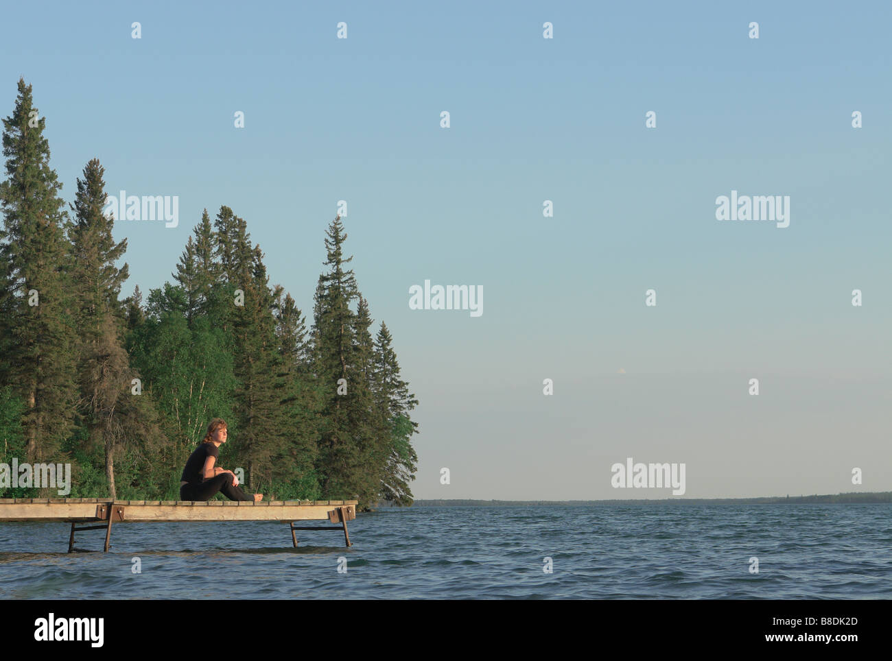 Woman seated on dock by lake, Clear Lake, Riding Mountain National Park, Manitoba, Canada Stock Photo