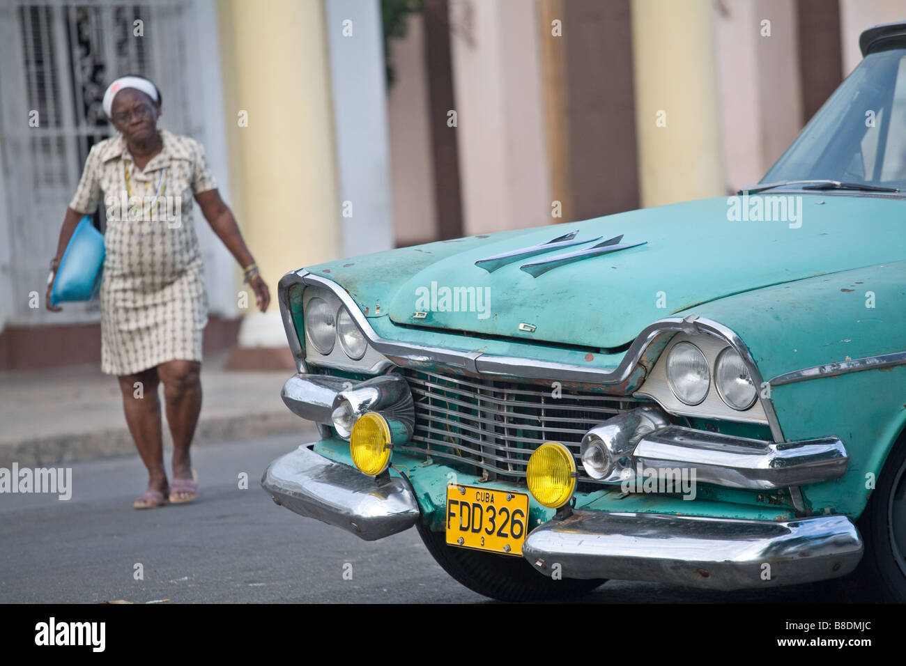 woman crossing street next to a green Dodge car in Cienfuegos, Cuba Stock Photo