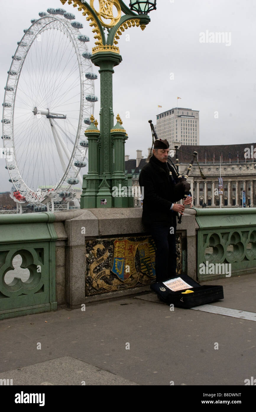 Man playing the bagpipes on Westminster Bridge with the London Eye in the background. Stock Photo