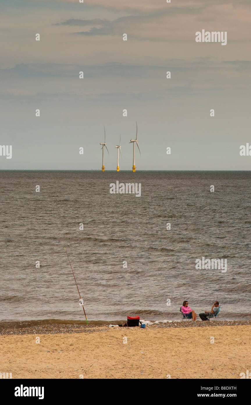Norfolk England Couple on the beach fishing with wind turbines out at sea Stock Photo