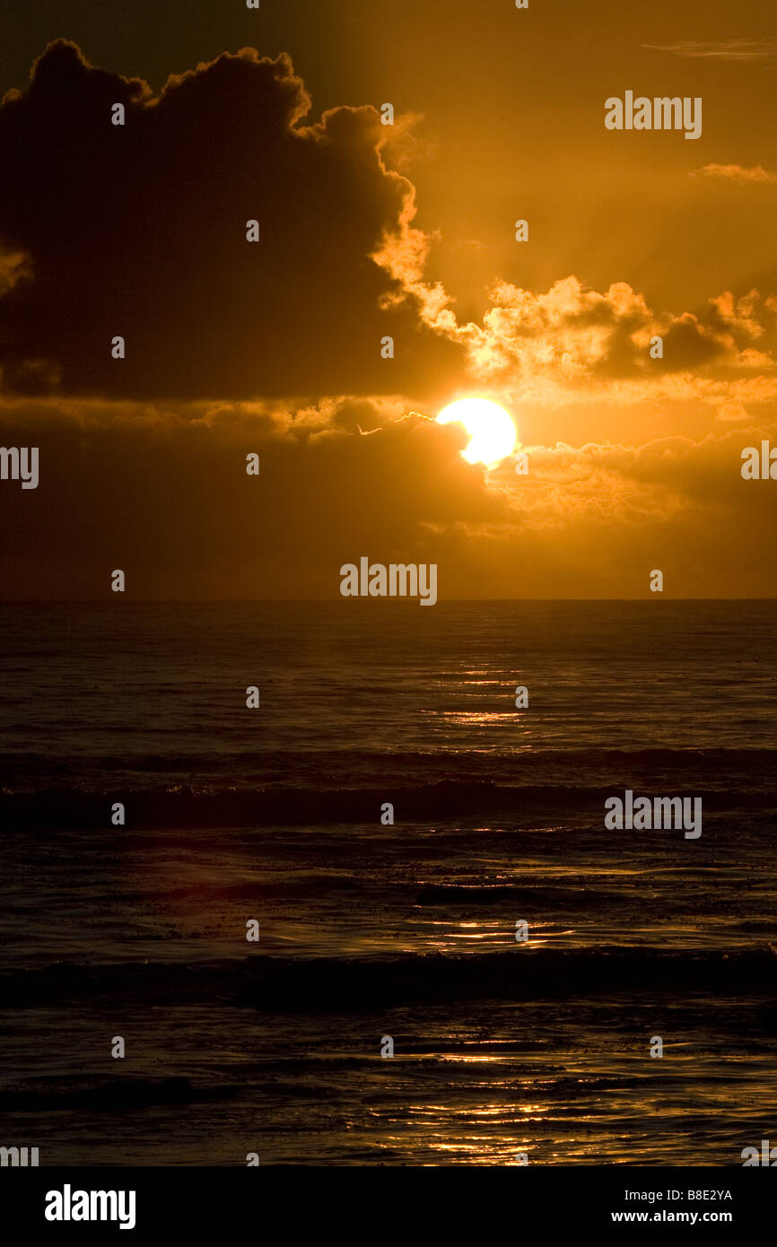 Setting Sun Peeking Out from Behind Clouds over Pacific ocean Stock Photo
