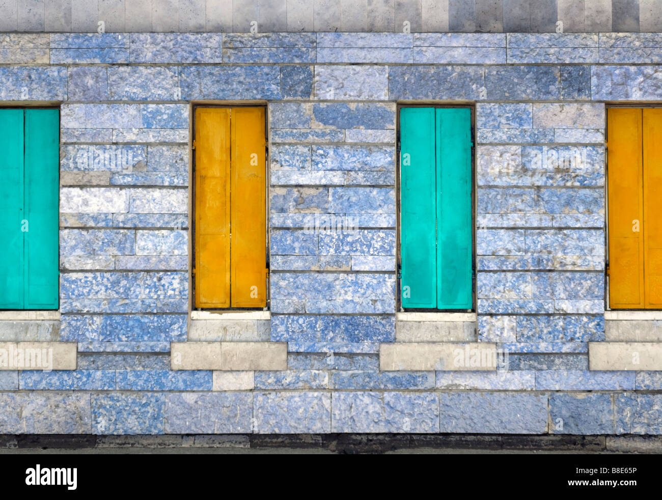 Four closed metal window shutters over stone covered wall. Stock Photo