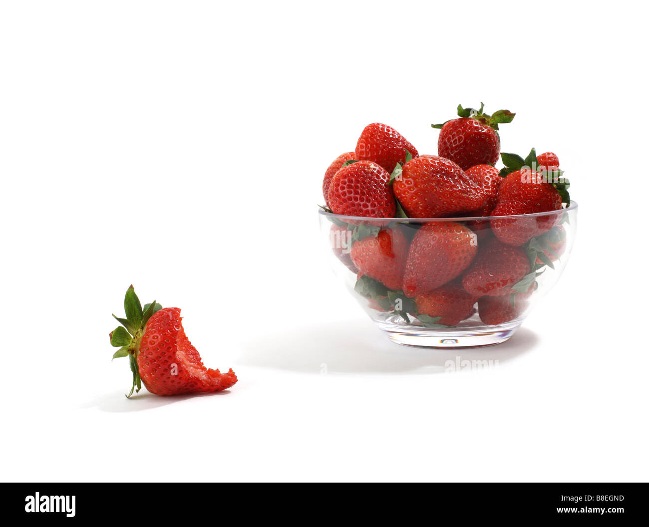 Clear Glass Bowl of Red Organic Strawberries one eaten in foreground Stock Photo