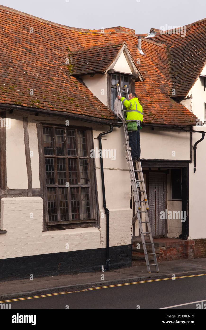 A window cleaner at work up a ladder wearing a high visibility coat in