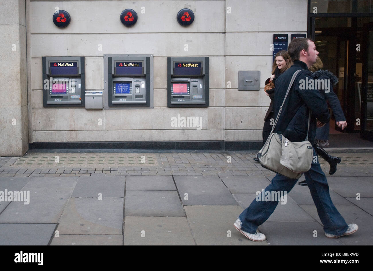 Man passing in front of NatWest cash dispensers Stock Photo