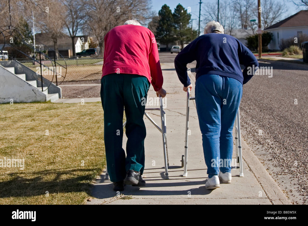 Two elderly senior citizens walk away using walkers, one of four in series Stock Photo