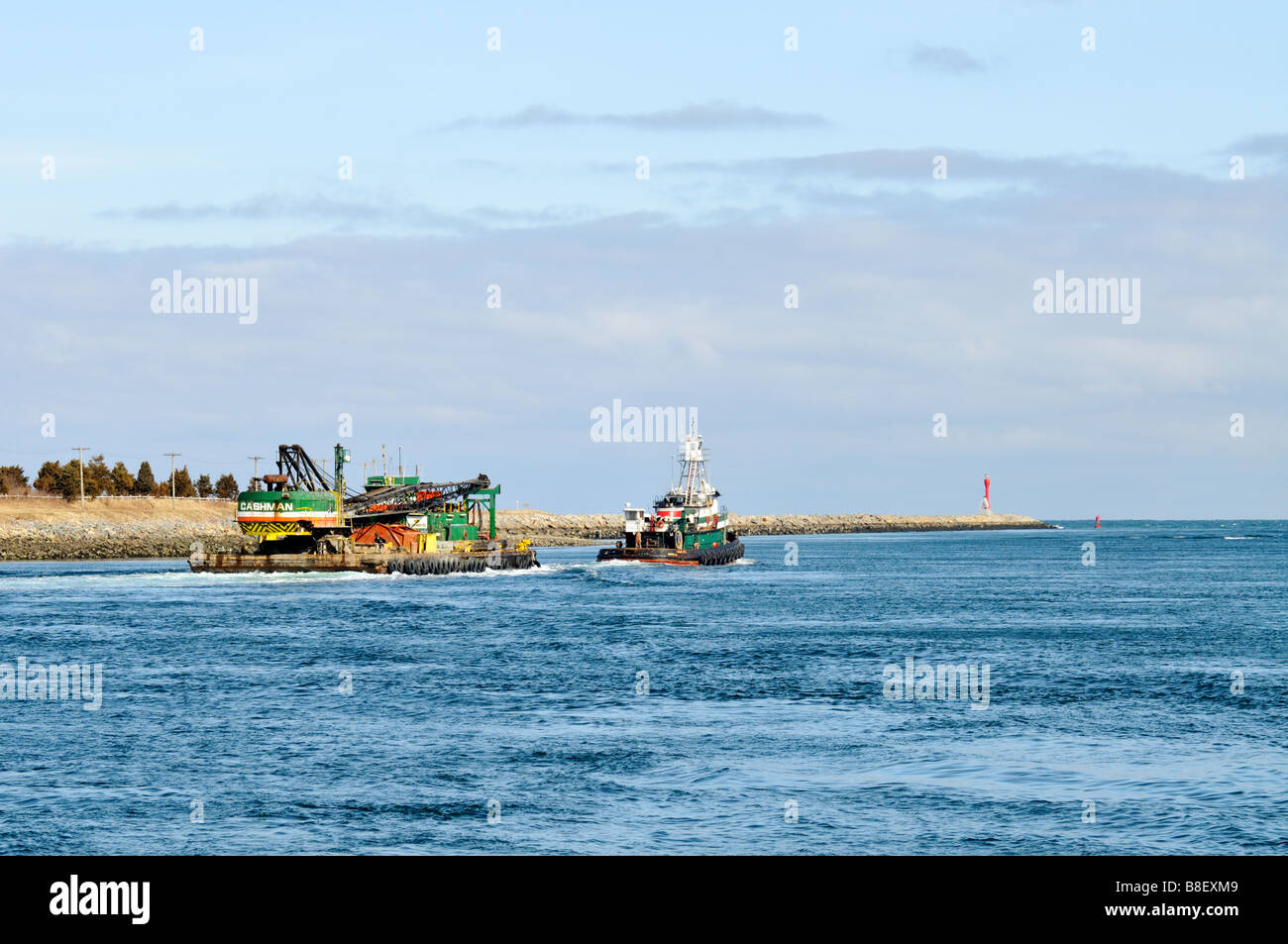 Tugboat pulling barge loaded with a crane heading out to sea by the jetty in the 'Cape Cod Canal' Stock Photo