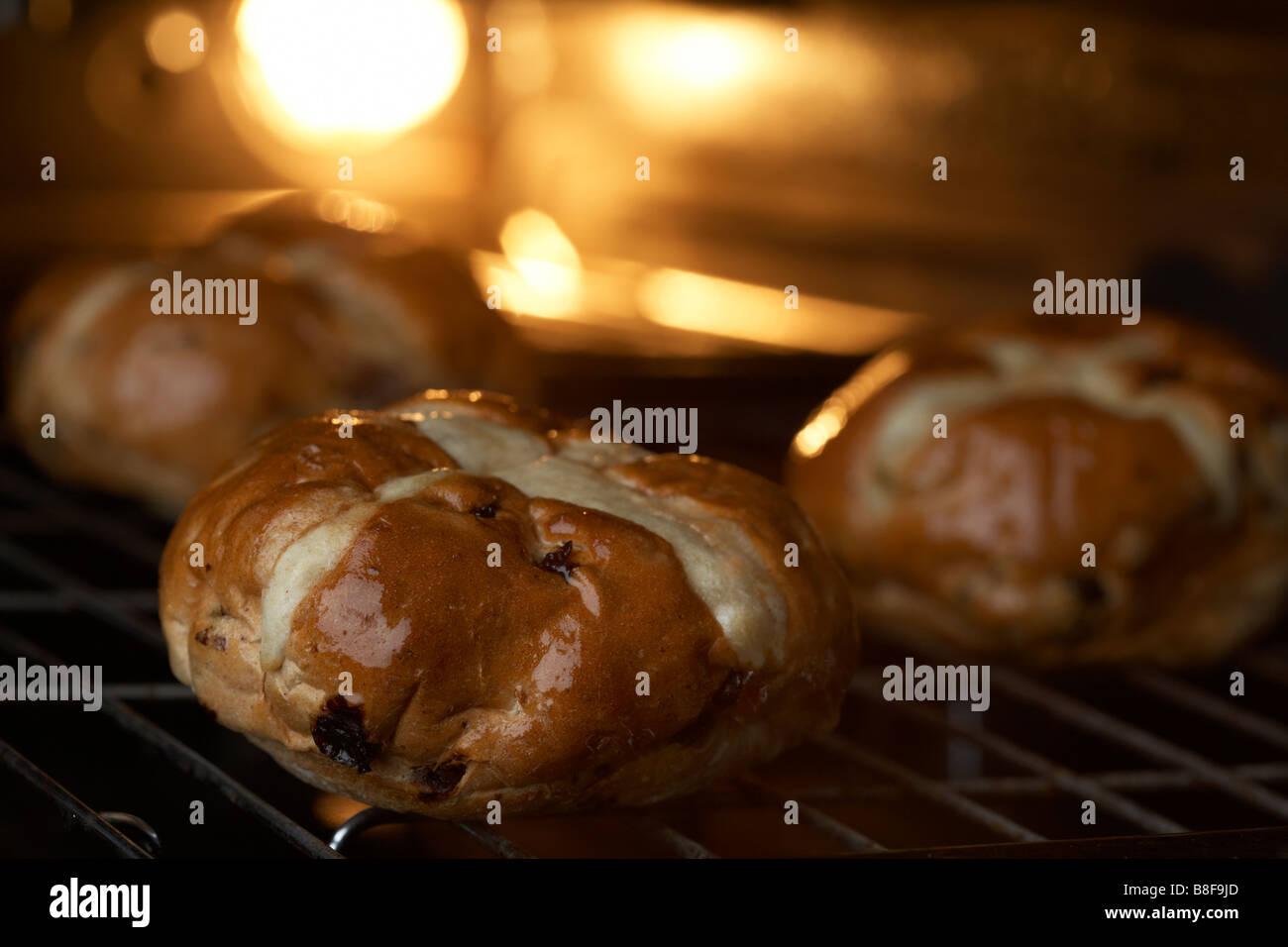 three hot cross buns sitting on a grill tray in the oven being heated Stock Photo