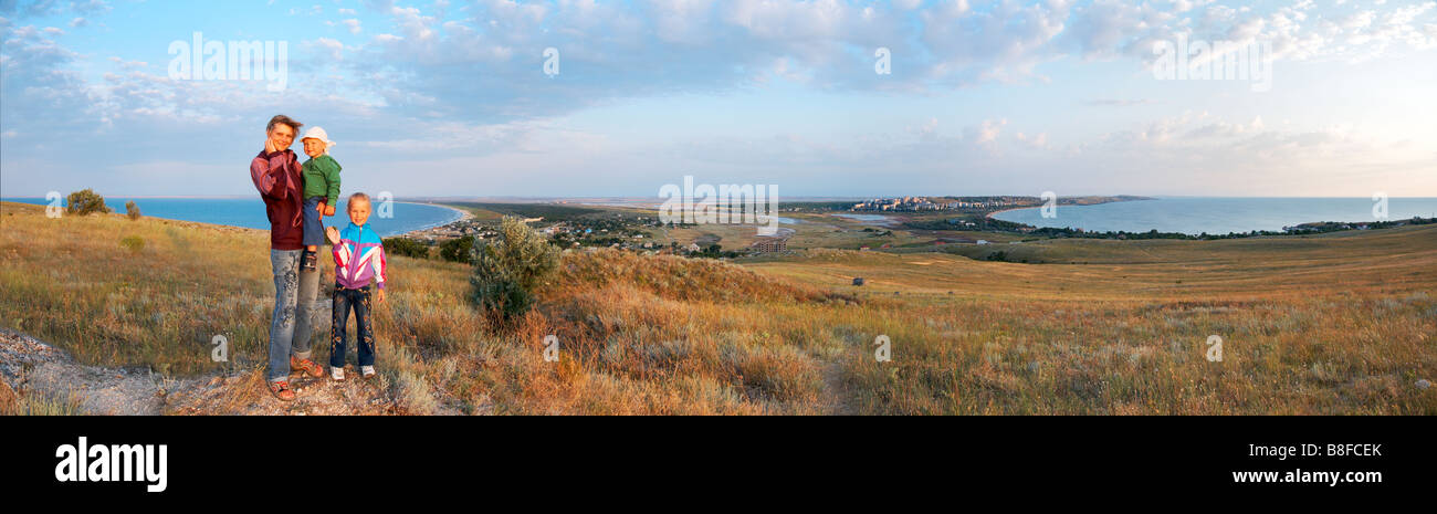 Mother with small girl and boy on evening prairie and sea coast behind. Stock Photo