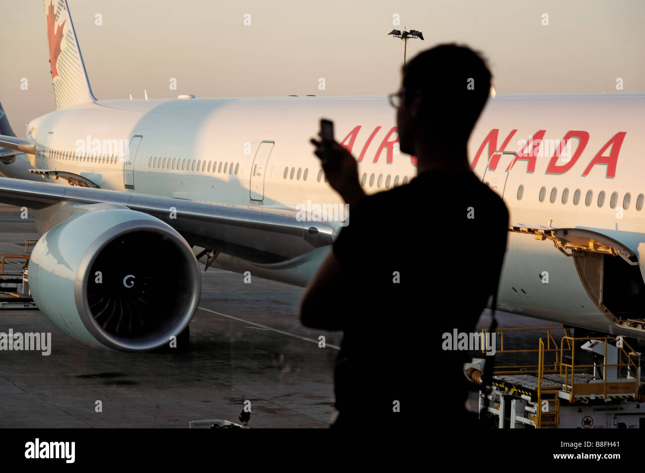 A man on a mobile phone in silhouette in an airport departure lounge window with a plane behind Stock Photo