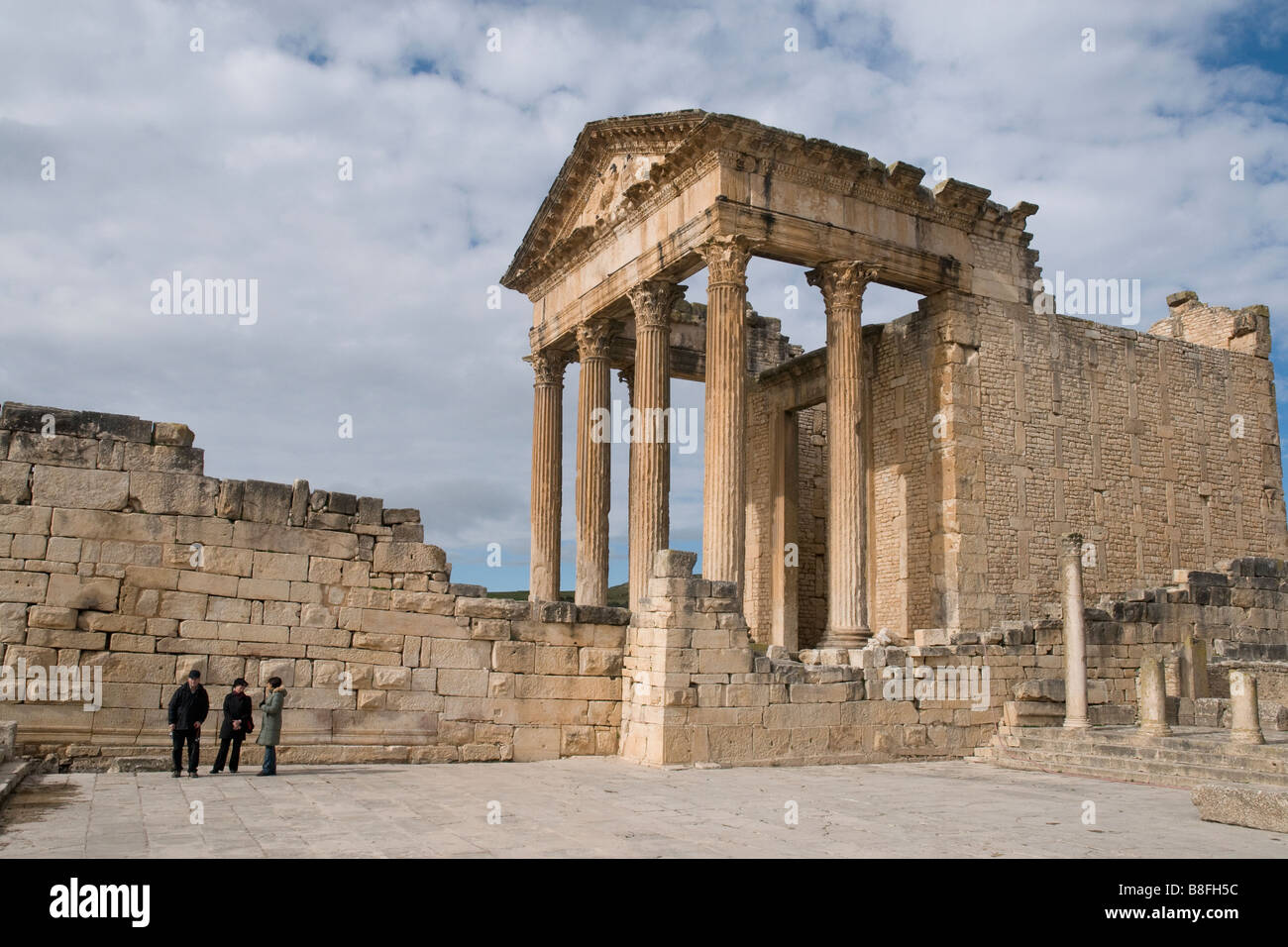 Among Tunisia's Roman ruins is Dougga with its splendid Capitol. Three visitors look small in the forum beside it. Stock Photo