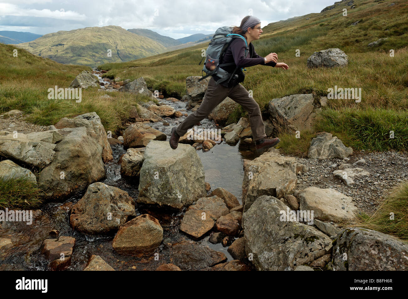 A young woman jumping across a river on stepping stones Stock Photo