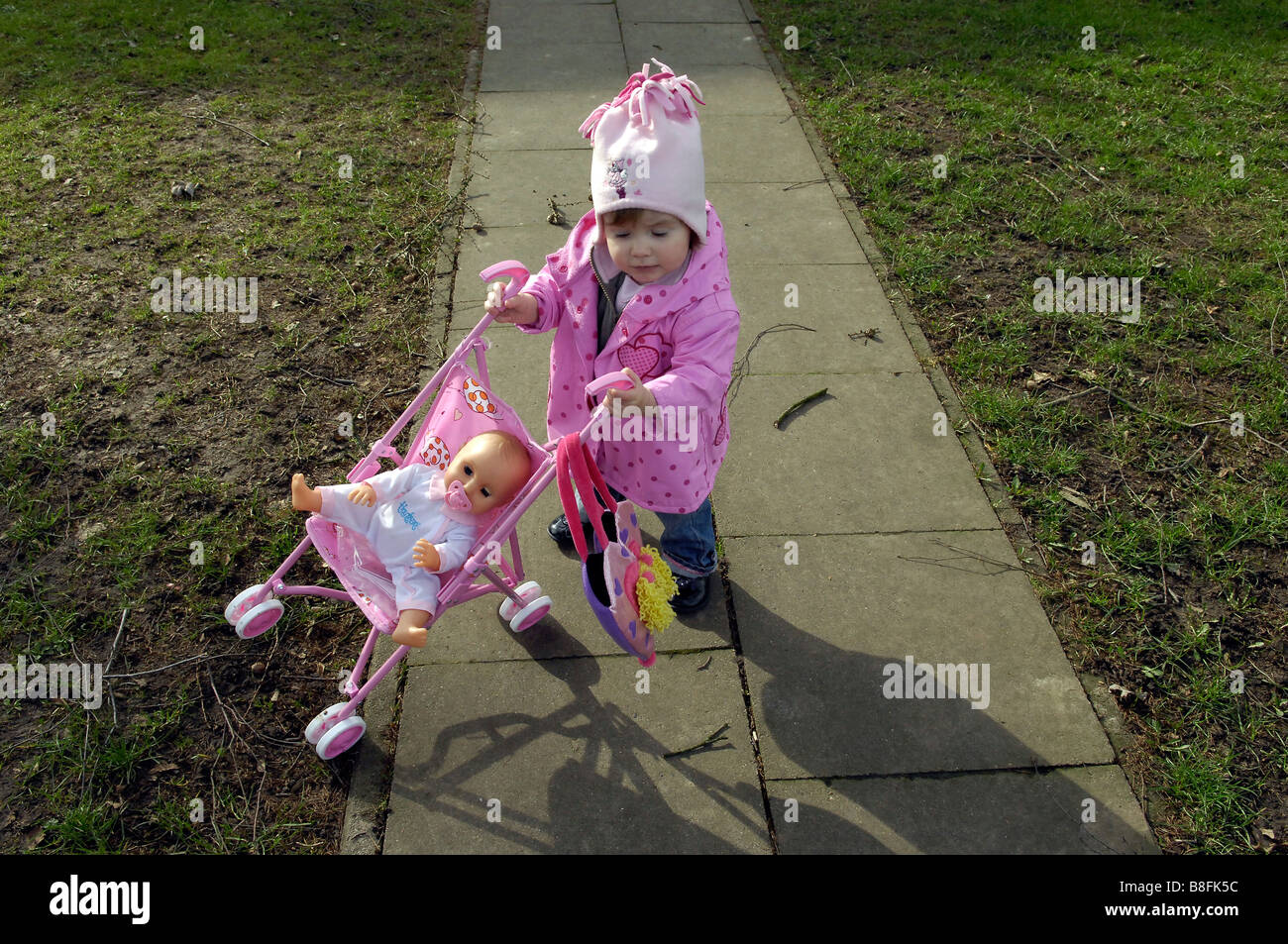 toddler girl pushing dolly in toy pram outside Stock Photo
