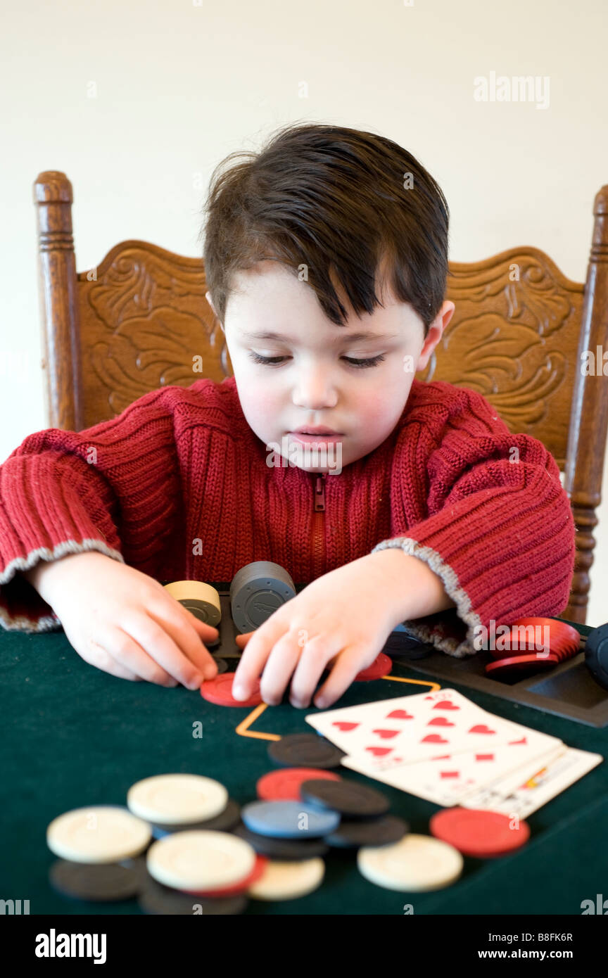 Young child holds a full house hand of poker and pulls in his chips Stock Photo