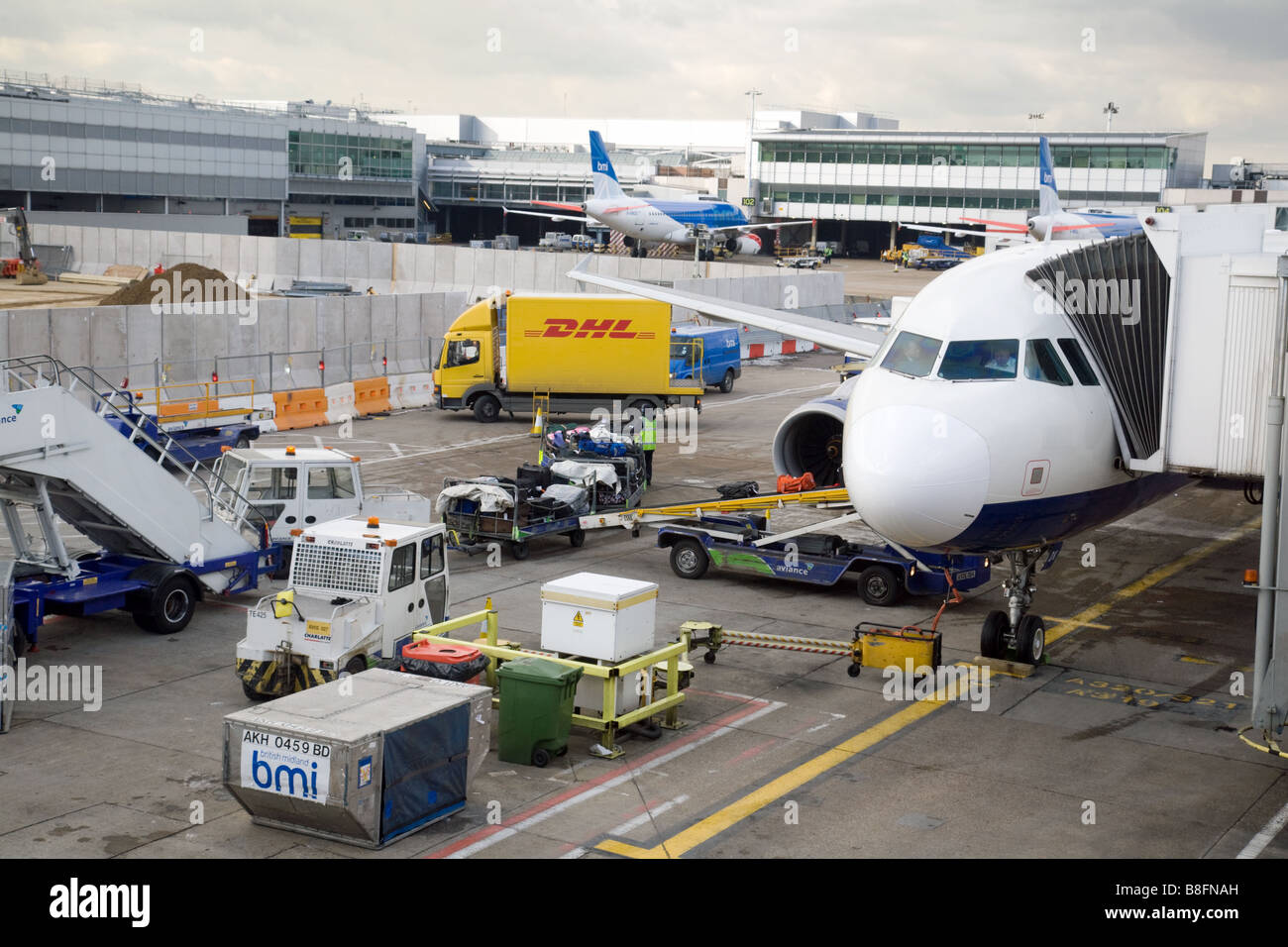 Baggage handlers and vehicles around a A BMI plane on the tarmac at Terminal 1, Heathrow airport, London, UK Stock Photo
