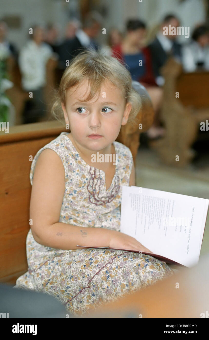 Little Girl with a Songbook in her Lap sitting on a Bench in a Church Ceremony Baptism