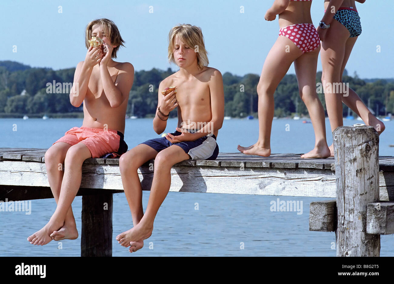 Two Boys with naked Torso eating Bread while two Girls in Bikini walk by -  Snack - Leisure Time - Friendship - Lake Stock Photo - Alamy