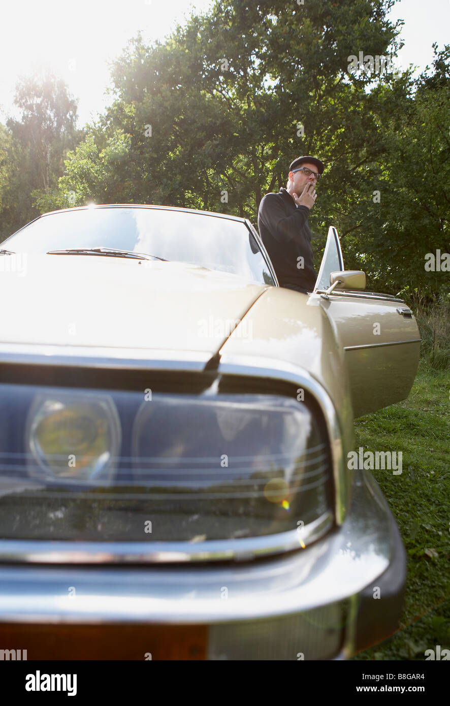 man in black clothes smoking a cigarette next to a vintage car in the countryside Stock Photo