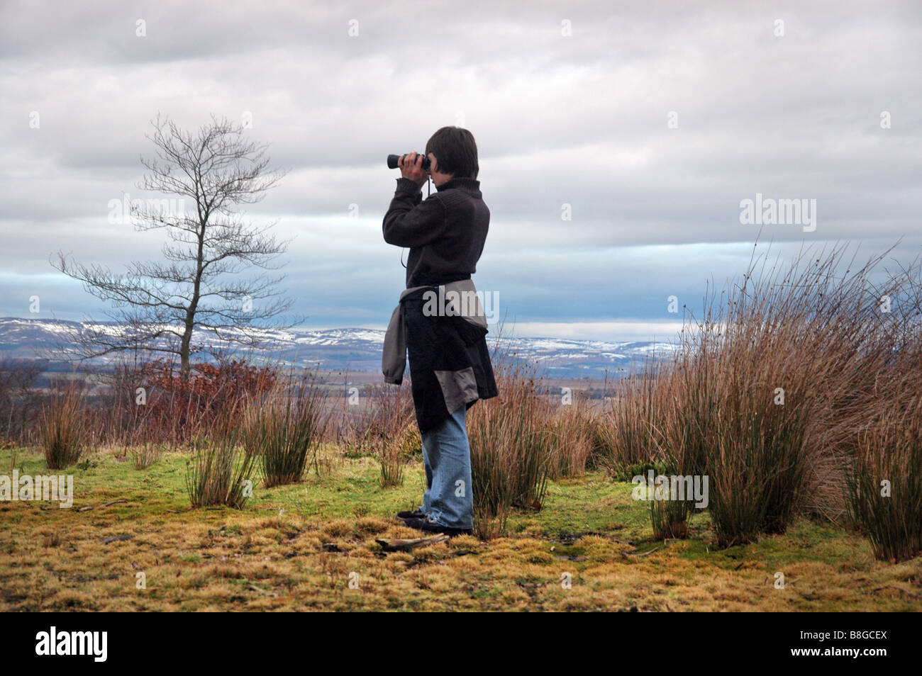 A teenage boy bird watches using binoculars. Stock Photo