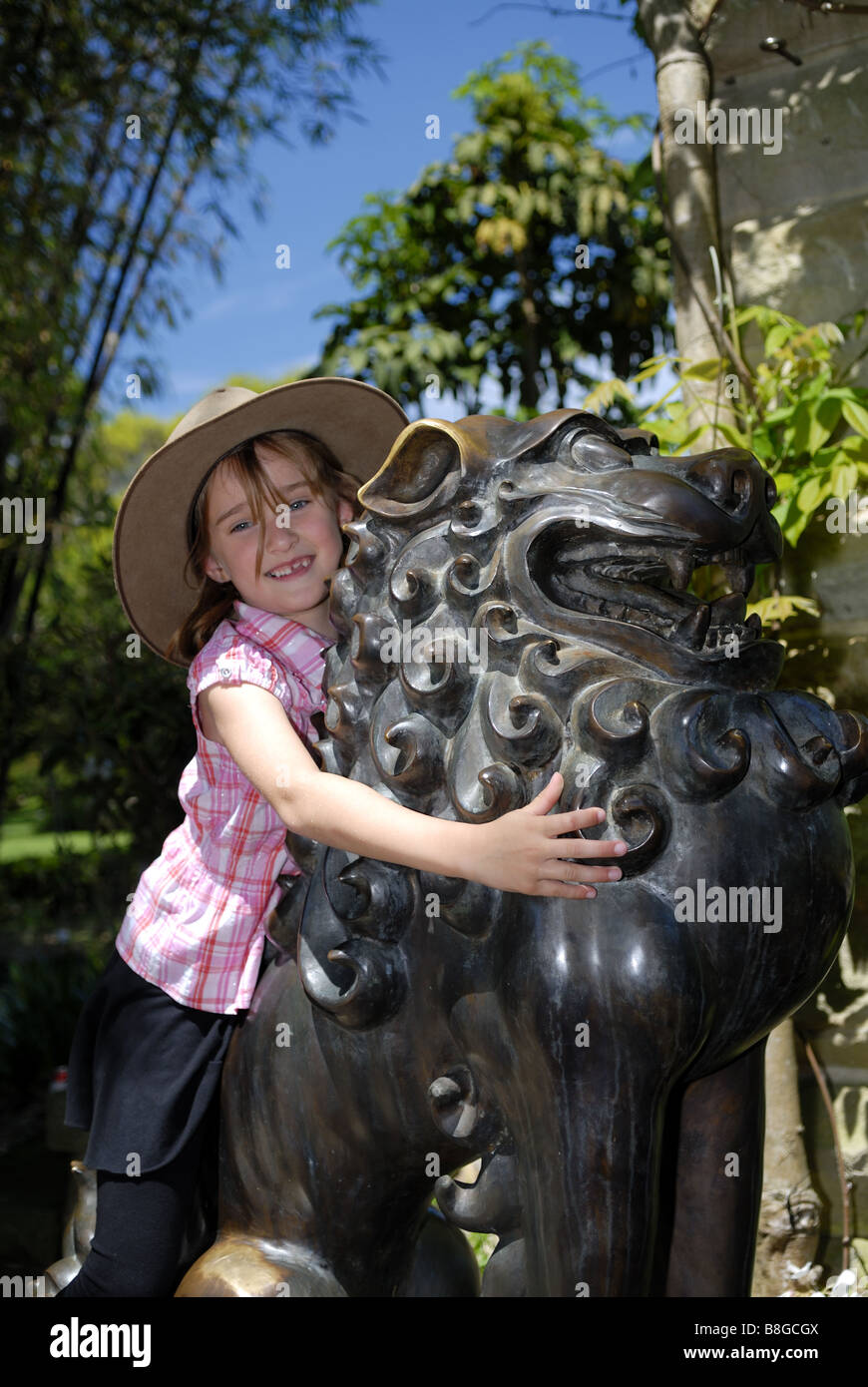 Child (6 years old) playing on one of two bronze lions, known as Temple Dogs, in Royal Botanic Gardens. Sydney, Australia Stock Photo