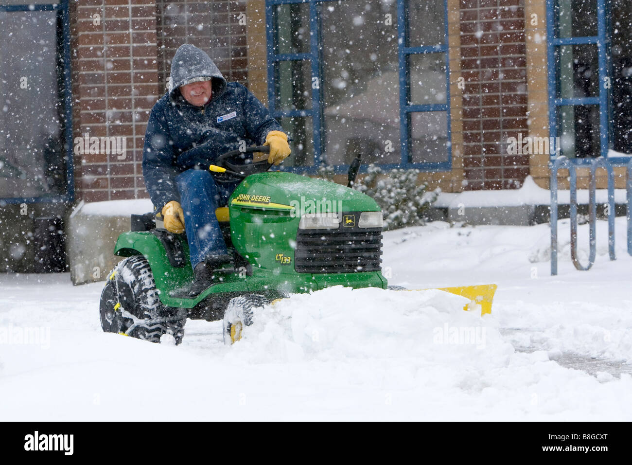 John Deere riding lawn mower fitted with a snow plow removing snow from a parking lot in Boise Idaho USA Stock Photo