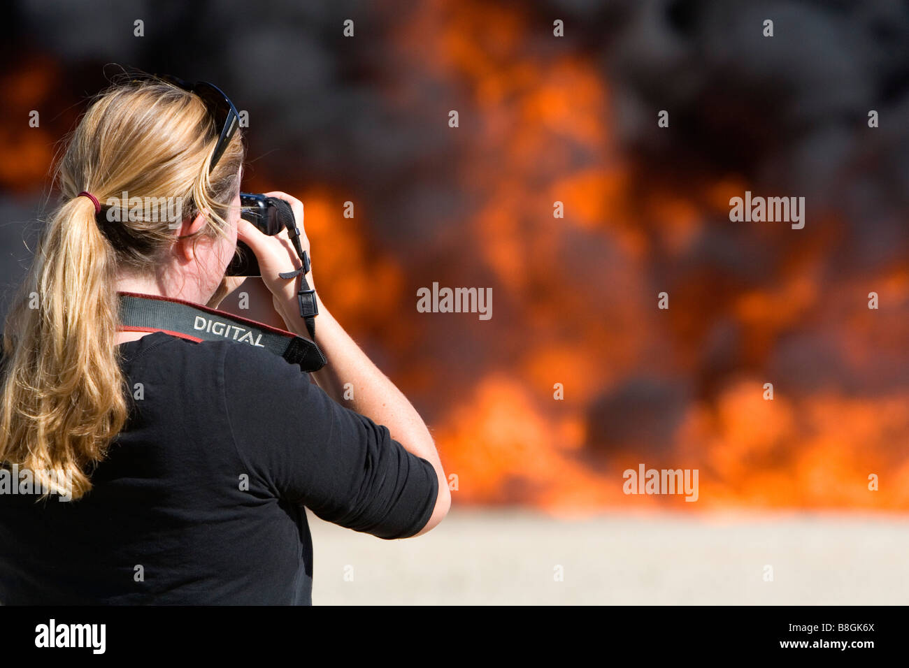 Female photographer taking digital photos of a jet fuel fire at a