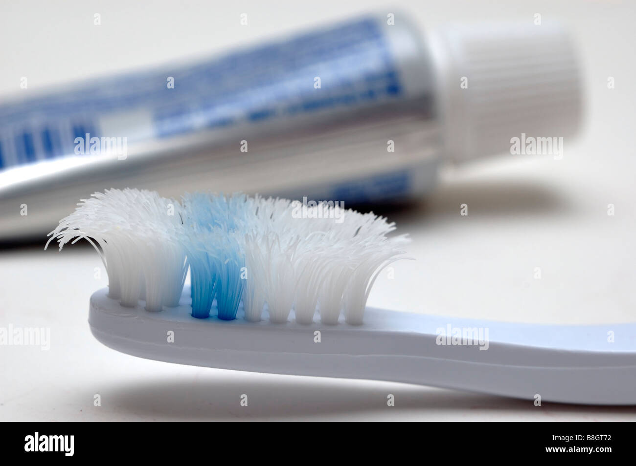 Closeup of a very worn toothbrush with a tube of toothpaste in the background Stock Photo