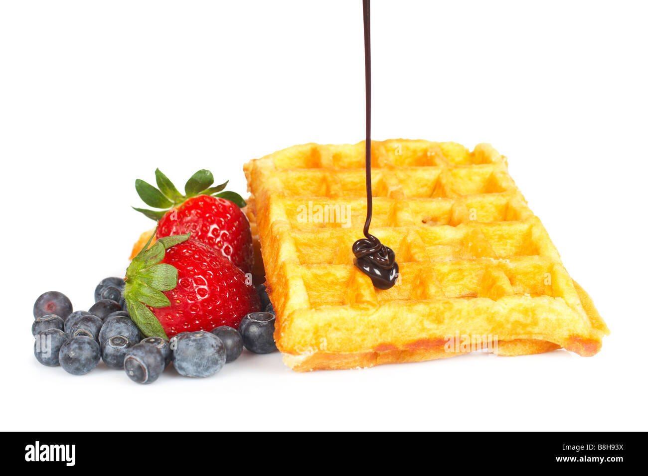 Chocolate syrup being poured over a waffles with blueberries and strawberries on a white background Stock Photo