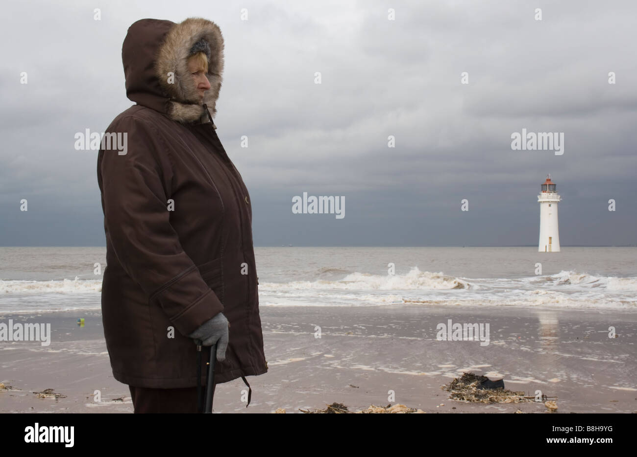 A woman of retirement age with a walking stick looking out to sea next to Fort Perch Rock Lighthouse New Brighton Stock Photo