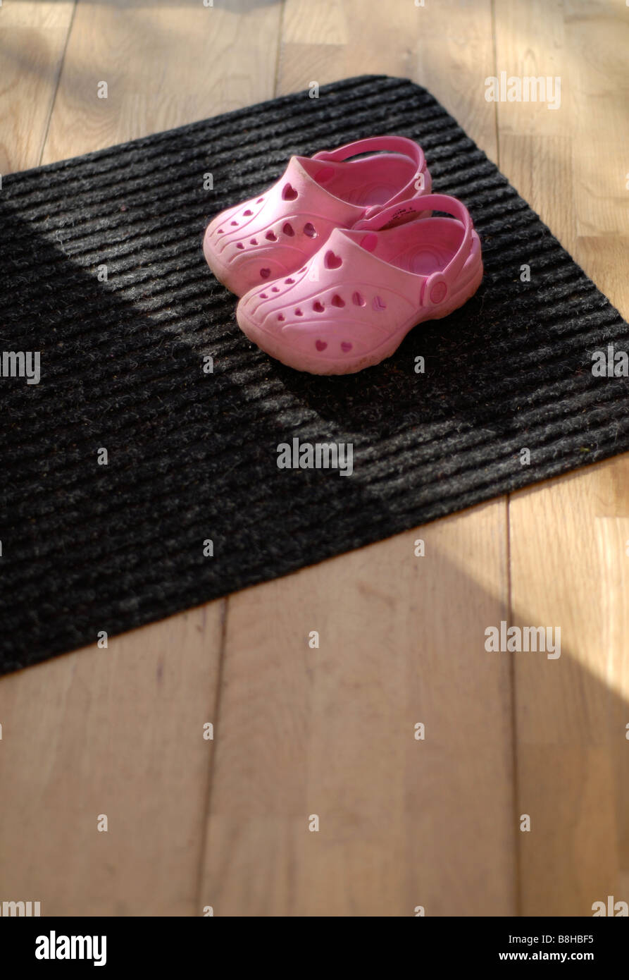 Childs pink croc style outdoor play shoes sitting on the door mat by an  open door Stock Photo - Alamy