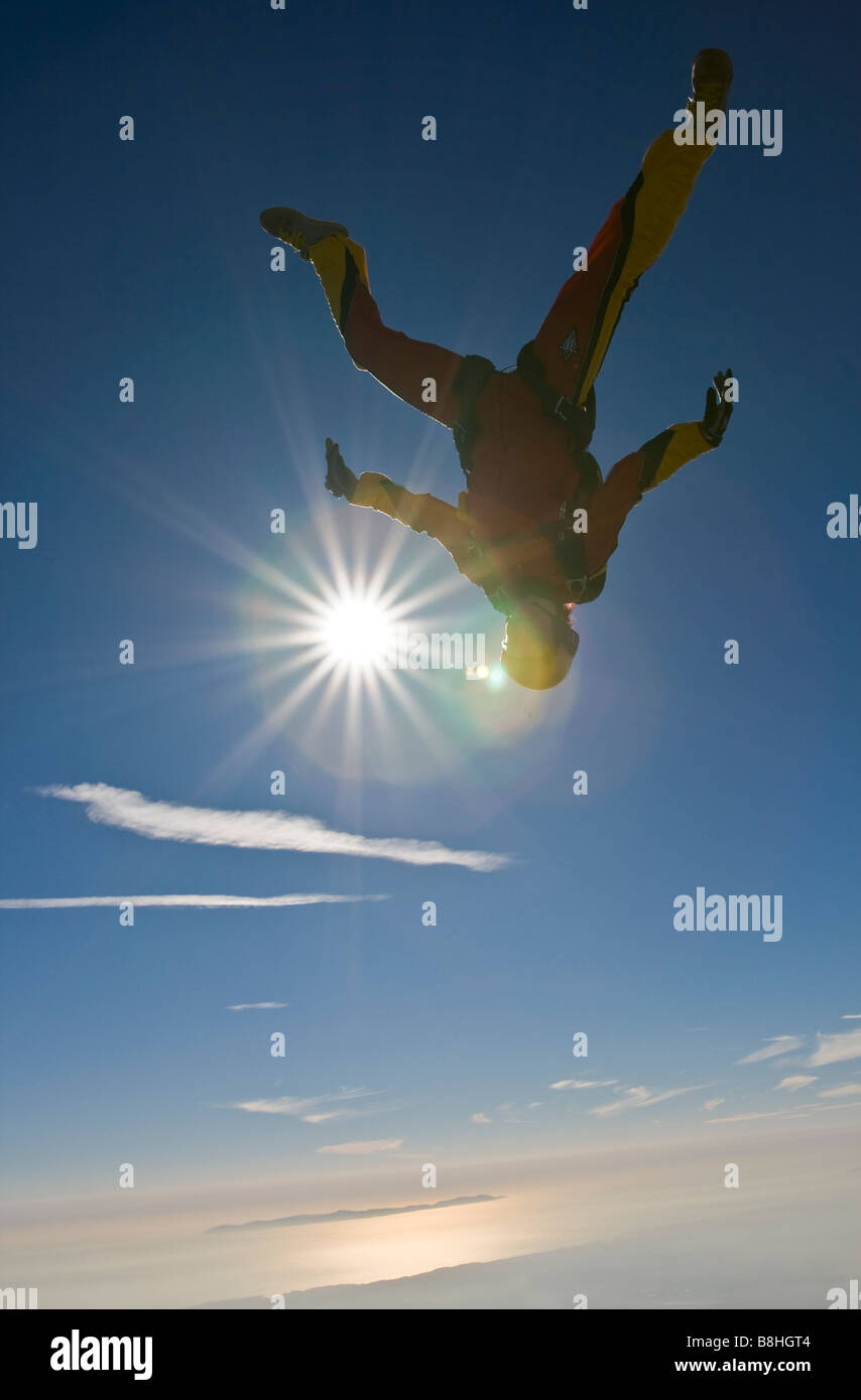 Skydiver is head down flying in the blue sky over a big lake and having fun. The clouds line in ...
