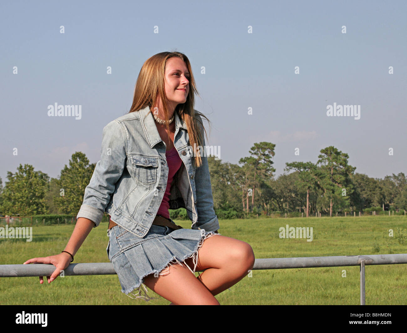 A beautiful girl sitting on a fence in the country looking toward ...