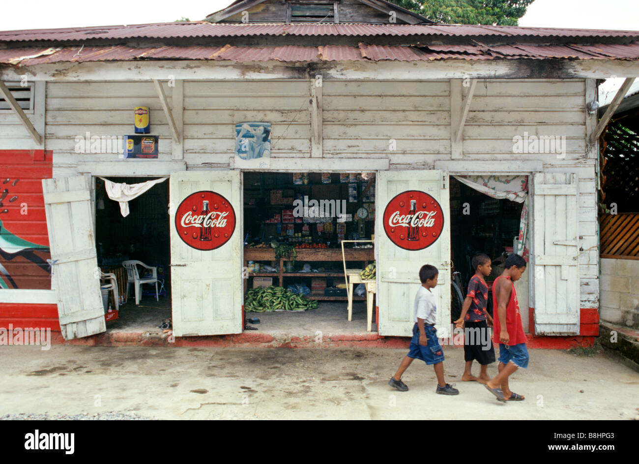 Three children boys walk by a corner store with Coca-cola advertisement in the Garifuna town of Livingstone Guatemala Stock Photo