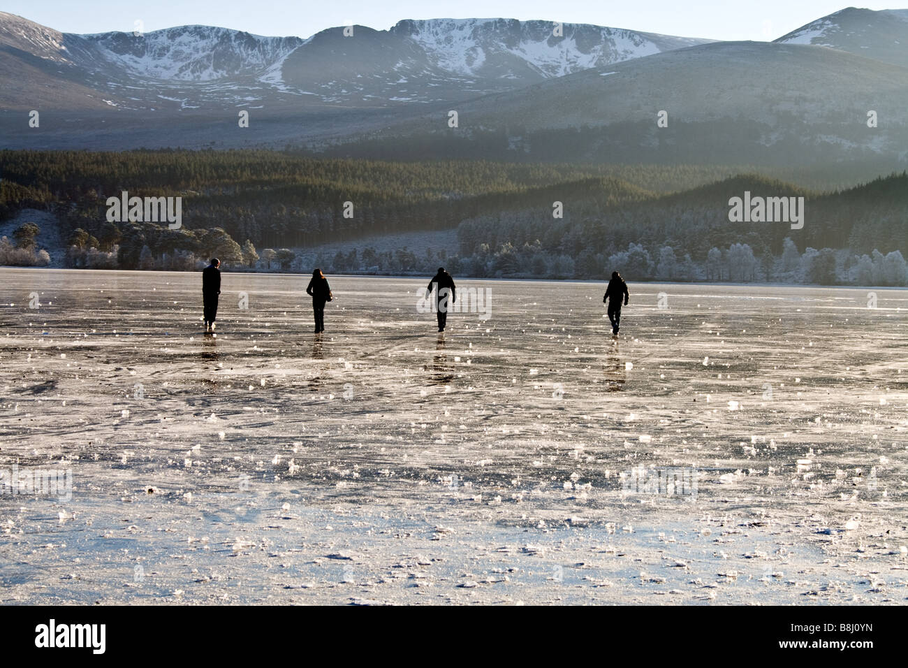 4 people walking on the ice in Loch Morlich near the Cairngorm mountains in the highlands of Scotland Stock Photo