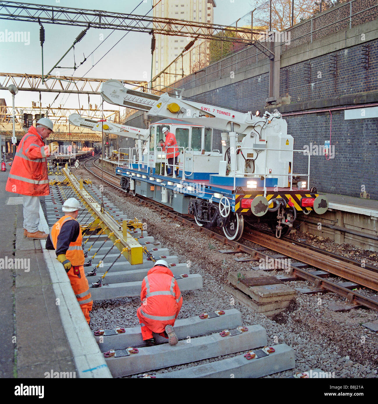 Self-propelled twin-jib rail crane lifts concrete sleepers into position at mainline station during a track renewal programme. Stock Photo