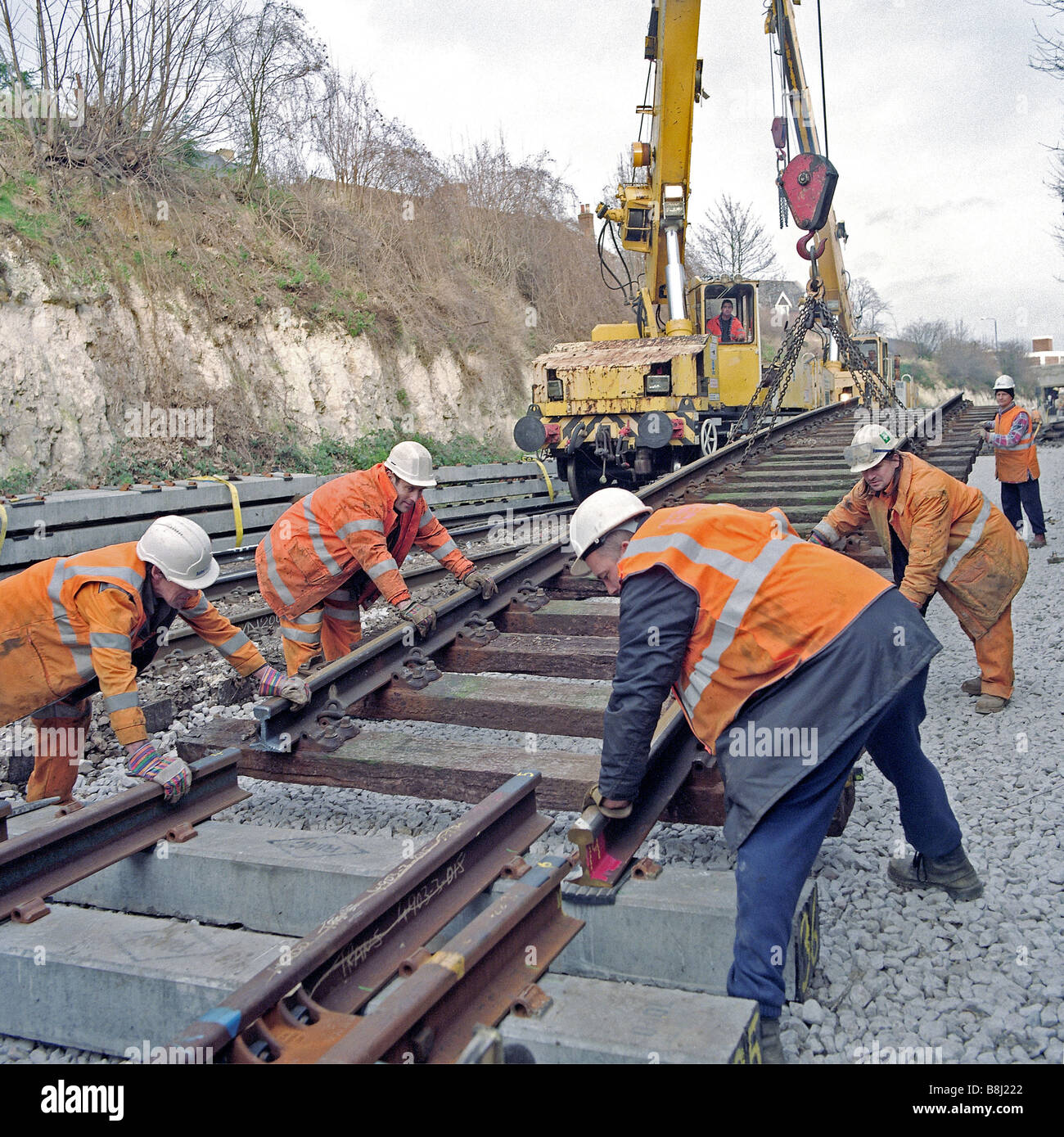 Contractors using rail crane lift redundant wooden-sleepered track panel before replacing with modern concrete equivalent. Stock Photo