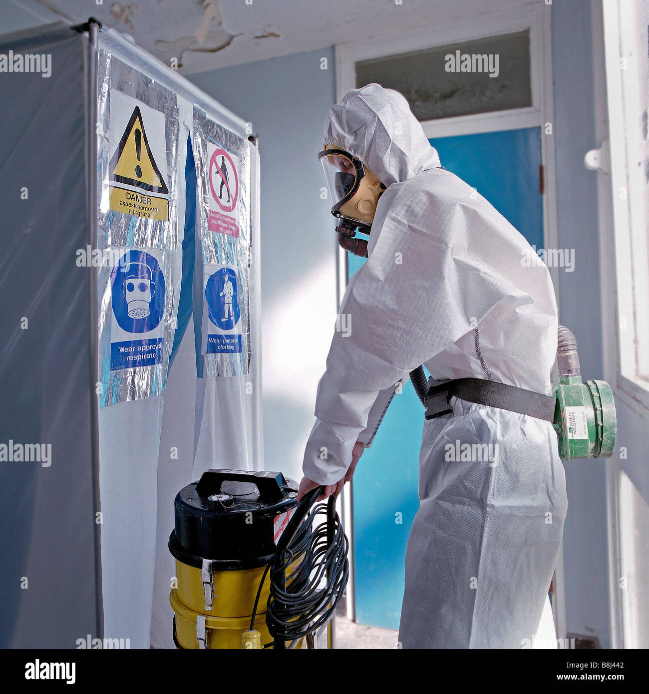 Licensed, trained and specially equipped operative enters building through air lock to remove toxic asbestos before demolition. Stock Photo